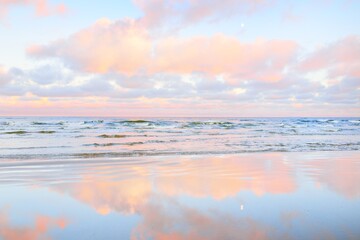 Sea shore at sunset. Clear blue sky, colorful glowing pink clouds, soft light. Symmetry reflections...
