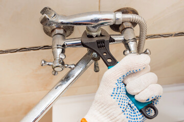 The plumber unscrews the nut of the broken water mixer in the bathroom with a wrench