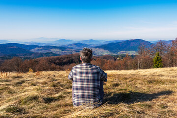 Rear view of lonely man sitting on grassy hill and looking at the mountains 