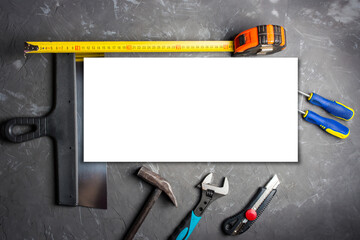 A mockup of construction tools against a background of dark concrete screwdriver, construction trowel, pliers, construction tape measure, hammer, office knife, adjustable wrench, template, 