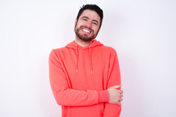 young Caucasian bearded man wearing pink hoodie against white background laughing.