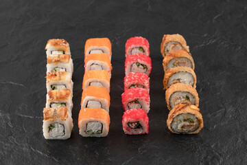 Set of delicious fresh sushi rolls on black surface