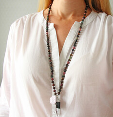 Rosary mala 108 beads from natural stones Tourmaline are worn on a girl in a white shirt. Author's jewelry from natural stones, Buddhism, matra, prayer, rosary from stones for prayer and beauty