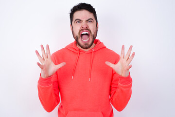 Fototapeta premium young Caucasian bearded man wearing pink hoodie against white wall crying and screaming. Human emotions, facial expression concept. Screaming, hate, rage.