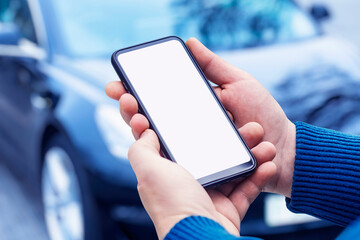Man holds a smartphone in his hands. Mock up phone with white screen on the background of the car.