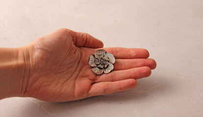 A flower brooch made of natural gray mother-of-pearl lies on a woman's hand. Author's jewelry. Designer elegant jewelry