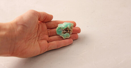Natural chrysoprase stone is on a woman's hand, in the palm of her hand, on a light background. Natural stones, crystals for magic, lithotherapy, geology, minerals, stone collection