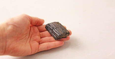 Natural black tourmaline sherl stone is on a woman's hand, in the palm of her hand, on a light background. Natural stones, crystals for magic, lithotherapy, geology, minerals, stone collection