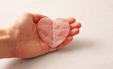 Natural rose quartz heart stone is on a woman's hand, in the palm of her hand, on a light background. Natural stones, crystals for magic, lithotherapy, geology, minerals, stone collection