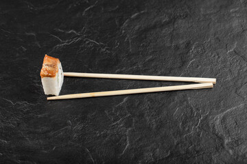 Single dragon sushi roll with chopsticks on black background