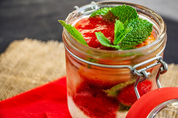  cooling strawberry cocktail with ice cubes and mint on black and red background and burlap napkin, stylish and tasty