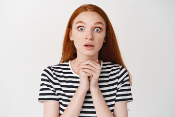 Close-up of excited redhead girl excepting something, looking with anticipation and hope at camera, standing over white background