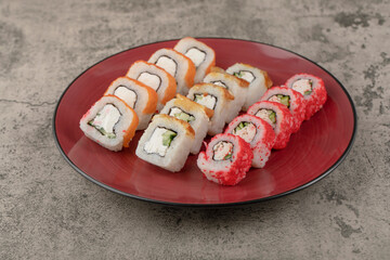 Red plate of various delicious sushi rolls on marble background