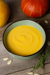 Pumpkin cream soup in green bowl on a wooden table in rustic style. Pumpkins, pumpkin seeds and rosemary branches on the table