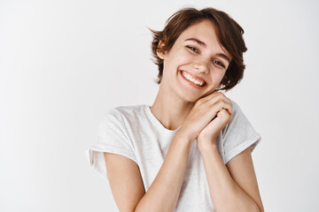 Fototapeta premium Portrait of candid happy woman with short hair, looking at something adorable and cute, smiling cheerful at camera, white background