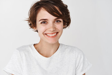 Close up portrait of cute girl with short hairstyle and clean smooth skin, smiling happy at camera,...
