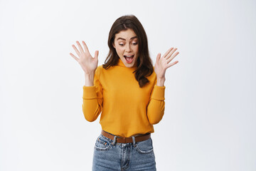 Excited girl screaming of fantastic news, gasping and raising hands up, looking down at amazing thing, checking out promo offer, standing against white background