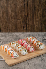 Wooden board of various sushi rolls on marble table