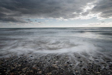 Seawaves splashing to the coast with stones against stormy dramatic cloudy sky. Wintertime, Limassol cyprus