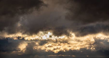 Dramatic clouds after the rain, illuminated by the setting sun against the backdrop of the evening sky. Sun rays passing through the clouds