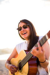 Fototapeta premium Young Latin woman play acoustic guitar on the Corunna Beach in Galicia Spain. Enjoy the travel time on summer holidays playing outdoors and chill or relax