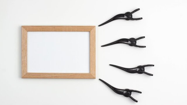 Stop motion animation mockup wooden frame flat lay of four black section hair clips of the right site of the image template with copy space on white background. Hairdresser salon equipment concept