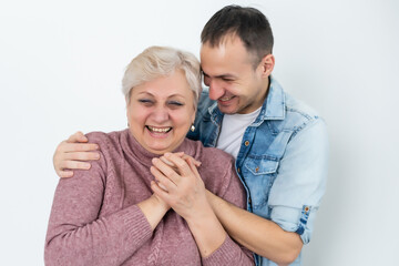 Head shot happy young bearded man embracing beautiful smiling middle aged senior mother in eyewear, relaxing together on comfortable sofa in living room, enjoying funny conversation or gossiping