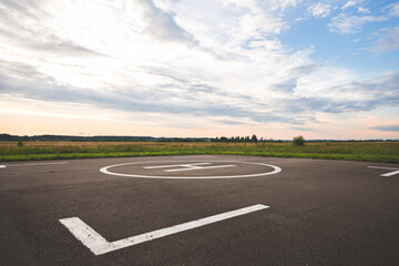 A large area with a special symbol in the center for helicopter landing. Private helipad in a green field against the backdrop of evening clouds.
