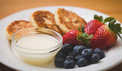 Closeup on a plate with delicious cheese cakes, strawberries, blueberries and sweet sauce on a wooden background. Healthy lifestyle concept