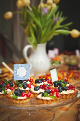 Closeup of homemade tartlets with organic blueberry and red currant vanilla buttercream. Delicious sweet dessert for a party or celebration. Bouquet of tulips in the background