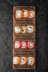 Wooden plate of traditional sushi rolls on black table
