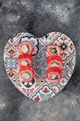 Obraz na płótnie Canvas Tasty sushi rolls with red caviar on heart-shaped plate