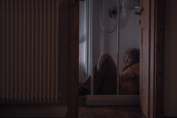 Distressed or deranged man dressed sitting in the shower traumatizing and being all drunk or stoned looking. Man with problems lying in the shower.