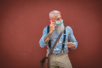 an older man in hipster clothes and glasses and a long white beard walks around talking on the phone focus on head