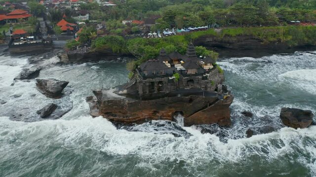 Overhead aerial rotating view of stunning buildings in Tanah Lot temple on a dark ocean cliff in rough sea in Bali, Indonesia