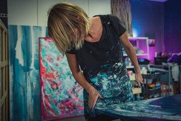 Young woman paints an abstract picture with her hands and spatula on a work table in her interior studio. Focus on head