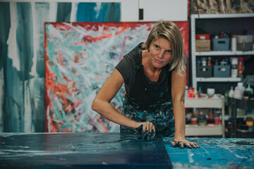 Young woman paints an abstract picture with her hands and spatula on a work table in her interior studio. Focus on head