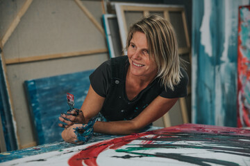 Young woman paints an abstract picture with her hands in her interior studio, focus on head