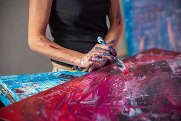 Young woman paints an abstract picture with her hands in her interior studio, focus on hand