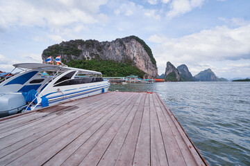 Travel by Thailand. Wooden pier with moored speedboat on sea lagoon with rock and cliffs.