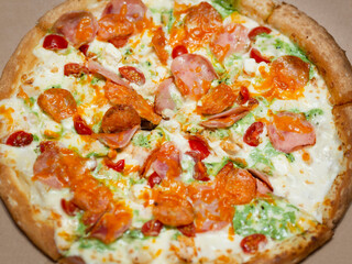 Traditional Italian fast food. Pizza with green pesto sauce, bacon, sausage, meat, ham, chicken, tomatoes, cheese, herbs and spices on a thin dough with sides. The concept of obesity, unhealthy food.