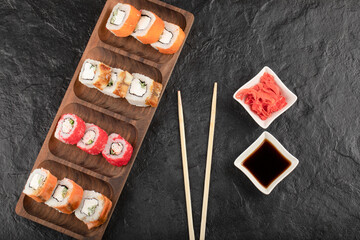 Wooden plate of traditional sushi rolls and pickled ginger on black table