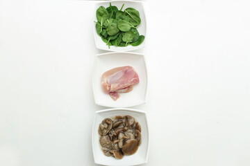 Isolated on a white background there are 3 white plates with different types of animal and vegetable. Plates include fresh green spinach leaves, chicken and pickled mushrooms. Have place for text