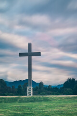 Fototapeta na wymiar Huge cross in a park with some green trees, on a cloudy day and some hills in the background 