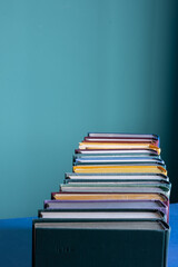 A slender row of second-hand books in hard fabric multi-colored covers. Bright green background. Vertical orientation.
