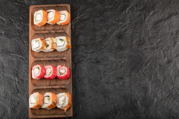 Wooden plate of traditional sushi rolls on black table