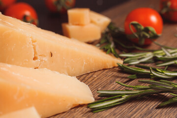 Pieces of hard, aged cheese parmesan, fresh tomatoes and herbs on wooden board