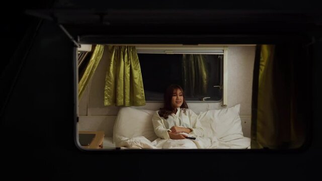 young woman using remote and watching TV in bed of a camper RV van motorhome at night