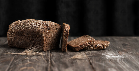 Sliced rye bread on a wooden dark background with copy space. Whole grain rye bread with sesame seeds and seeds.	