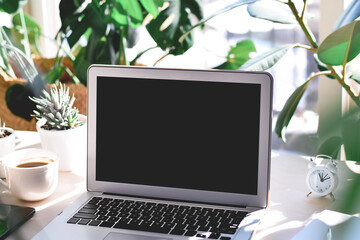 Fototapeta premium Workspace with laptop computer, notebook, cup of coffee, tropical houseplants, bright sunshine